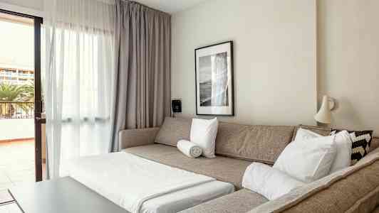 Oleskelutila, jossa vuodesohva, sohvapöytä ja parvekkeelle johtava ovi. (Tekoälyn luoma teksti)