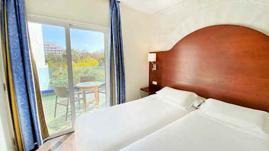 Hotellihuone, jossa on kaksi yhden hengen vuodetta, puinen pääty ja parveke, jossa on kaksi tuolia ja pöytä. (Tekoälyn luoma teksti)