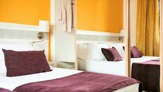 Hotellihuone, jossa on parivuode, violetit tyynyt ja oranssit seinät. (Tekoälyn luoma teksti)