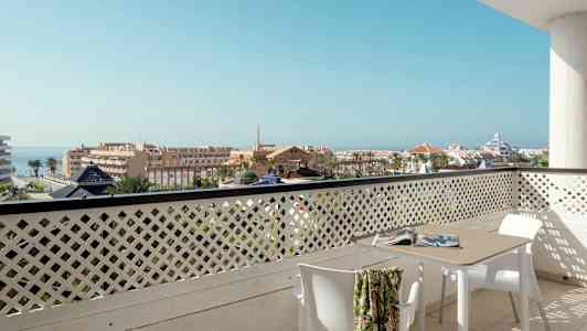 Näkymä parvekkeelta pöydän ja tuolien kanssa kaupunkimaisemaan, taustalla meri. (Tekoälyn luoma teksti)