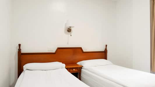 Kaksi yksittäissänkyä valkoisilla lakanoilla ja puisilla sängynpäädyillä vierekkäin. (Tekoälyn luoma teksti)