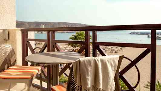 Parveke, jossa pöytä ja kaksi tuolia, näkymä rannalle ja merelle. (Tekoälyn luoma teksti)