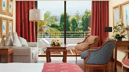 Hotellihuone, jossa kalusteita, kukkia ja näkymä vehreälle parvekkeelle. (Tekoälyn luoma teksti)