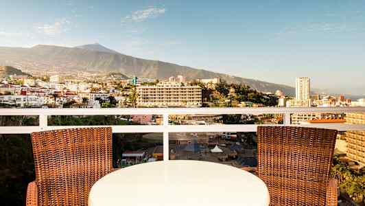 Pöytä ja kaksi tuolia parvekkeella, josta on näkymä kaupunkiin ja vuoristoon. (Tekoälyn luoma teksti)