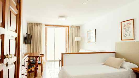 Huone, jossa on sänky, ruokapöytä, televisio ja lasiovet, jotka johtavat parvekkeelle. (Tekoälyn luoma teksti)