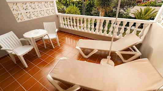 Terassi, jossa kaksi aurinkotuolia, pöytä ja kaksi tuolia, näkymä vehreisiin maisemiin. (Tekoälyn luoma teksti)