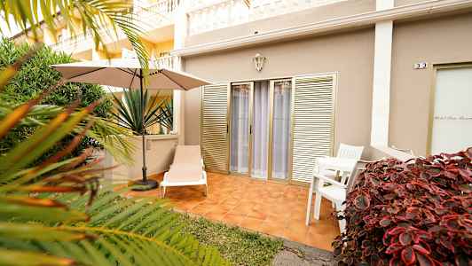 Ulkoterassi, jossa aurinkotuoli, varjo ja pöytä tuoleineen, ympäröivänä kasvillisuus. (Tekoälyn luoma teksti)