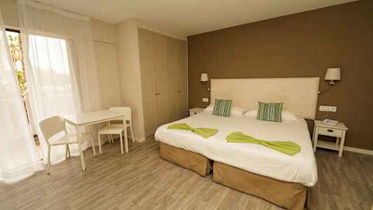 Hotellihuone, jossa on kaksi erillistä vuodetta, yöpöytä, pöytä, tuolit ja vaatekaappi. (Tekoälyn luoma teksti)