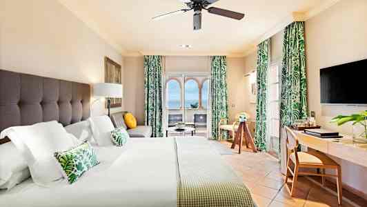 Hotellihuone, jossa on suuri sänky, istuma-alue, työpöytä ja merinäköala ikkunasta. (Tekoälyn luoma teksti)