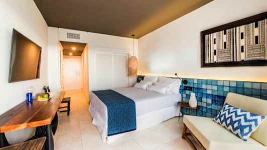 Moderni hotellihuone, jossa on parivuode, pöytä hedelmillä ja tuoli. (Tekoälyn luoma teksti)