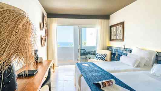 Valoisa hotellihuone, jossa on kaksi vuodetta, puupenkki ja parveke merinäköalalla. (Tekoälyn luoma teksti)