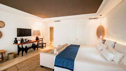 Moderni hotellihuone, jossa on suuri sänky ja istuinryhmä, sekä televisio ja pöytä kahvinkeittimellä. (Tekoälyn luoma teksti)