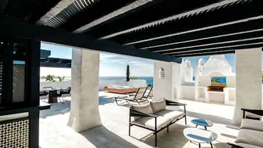 Aurinkoinen terassi, jossa on valkoiset seinät, mustat puupalkit ja modernit loungekalusteet. (Tekoälyn luoma teksti)