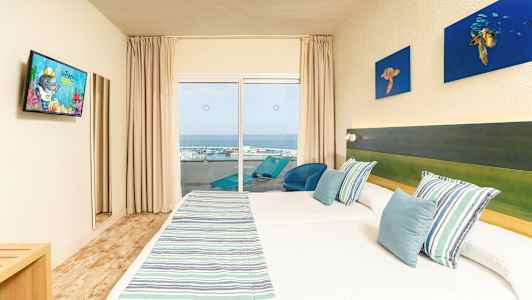 Hotellihuone, jossa kaksi sänkyä, raidalliset päiväpeitteet ja siniset tyynyt, parveke merinäköalalla. (Tekoälyn luoma teksti)