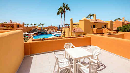 Terassi, jossa on pöytä ja tuolit, näkymä altaalle ja ympäröiviin rakennuksiin. (Tekoälyn luoma teksti)