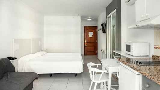 Hotellihuone, jossa parivuode, sohva, ruokapöytä tuoleineen ja minikeittiö. (Tekoälyn luoma teksti)