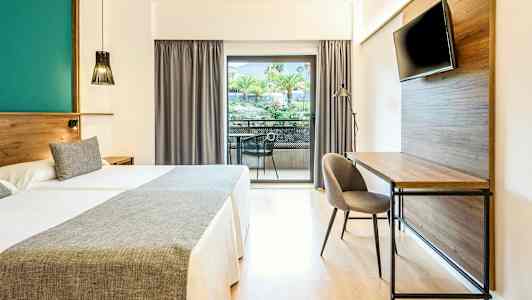 Hotellihuone, jossa on kaksi sänkyä, kirjoituspöytä, tv ja parveke, jolta on näkymä puihin ja viheralueisiin. (Tekoälyn luoma teksti)