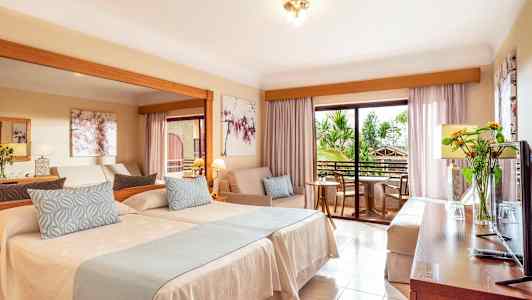 Hotellihuone, jossa on kaksi sänkyä, istuinryhmä ja parveke. (Tekoälyn luoma teksti)