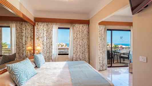 Hotellihuone, jossa on parivuode, koristeelliset tyynyt ja peili. Parveke merinäköalalla. (Tekoälyn luoma teksti)