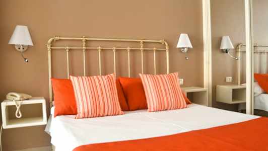 Hotellihuone, jossa sänky valkoisilla ja punaisilla vuodevaatteilla, ympäröitynä seinävalaisimilla. (Tekoälyn luoma teksti)