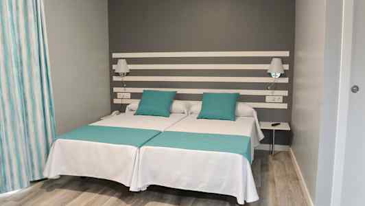 Kahden hengen huone, jossa kaksi erillistä vuodetta ja harmaa seinä. (Tekoälyn luoma teksti)