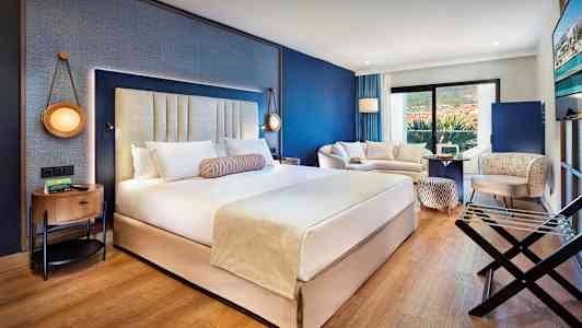 Moderni hotellihuone, jossa on suuri parivuode, oleskelutila ja parveke. (Tekoälyn luoma teksti)