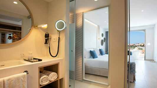 Hotellihuone, jossa on peili ja pesuallas makuuhuoneen vieressä, näkymä. (Tekoälyn luoma teksti)