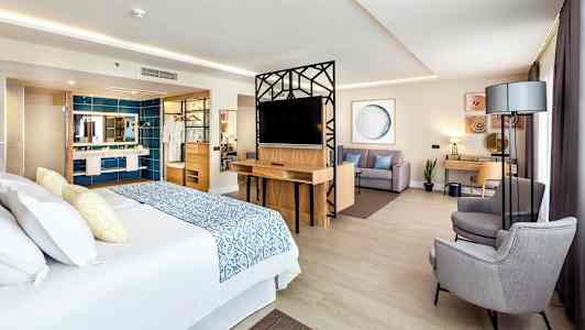 Hotellihuone, jossa on suuri sänky, oleskelutila ja kirjoituspöytä. (Tekoälyn luoma teksti)