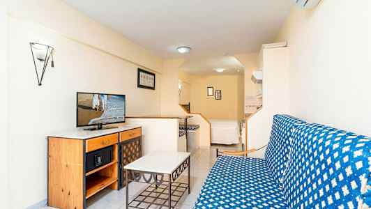 Studio, jossa on sohvaryhmä, pöytä ja lipasto, jolla on televisio. Taustalla on sänky. (Tekoälyn luoma teksti)