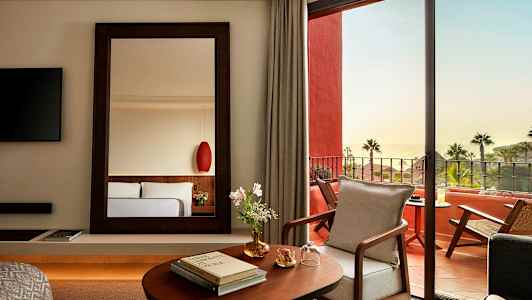 Tyylikäs hotellihuone, jossa on peili, avautumista kalustetulle terassille ja merinäköala. (Tekoälyn luoma teksti)