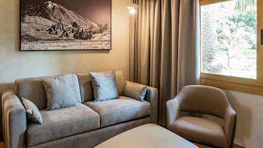 Olohuone, jossa harmaa sohva, beige nojatuoli, valkoinen pöytä ja kehystetty taulu seinällä. (Tekoälyn luoma teksti)