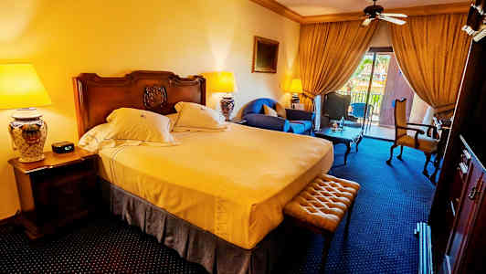 Hotellihuone, jossa on parivuode, istuimet ja parveke näkymillä. (Tekoälyn luoma teksti)