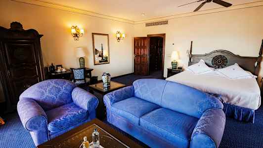 Hotellihuone, jossa parivuode, kaksi tuolia, pöytä ja lipasto, tyylikkäästi sisustettu. (Tekoälyn luoma teksti)