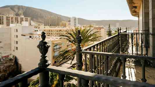 Parveke yksityiskohtaisilla rautakaiteilla, näkymät kaupunkirakennuksiin ja taustalla vuoristo. (Tekoälyn luoma teksti)