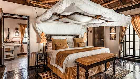 Tyylikäs makuuhuone, jossa on pylvässänky, ruskeita koristeita ja puulattia. (Tekoälyn luoma teksti)