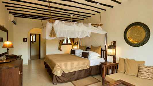 Hotellihuone, jossa on perinteinen sisustus, suuri sänky, jossa hyttysverkko, istuimet ja koristeita seinillä. (Tekoälyn luoma teksti)