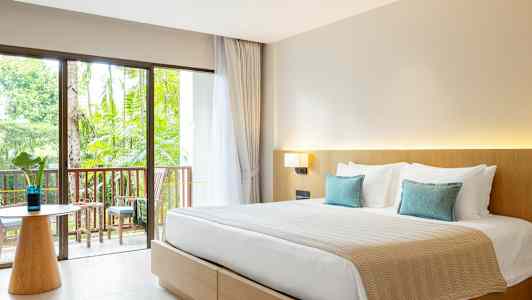 Hotellihuone, jossa on parisänky, vaaleat huonekalut ja parveke puutarhaan päin. (Tekoälyn luoma teksti)