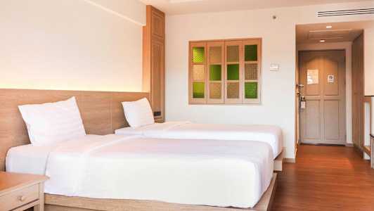 Kaksi yhden hengen sänkyä hotellihuoneessa, jossa on puulattia ja vaalea sisustus. (Tekoälyn luoma teksti)