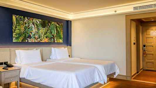 Hotellihuone, jossa on kaksi sänkyä ja värikäs taulu seinällä. (Tekoälyn luoma teksti)