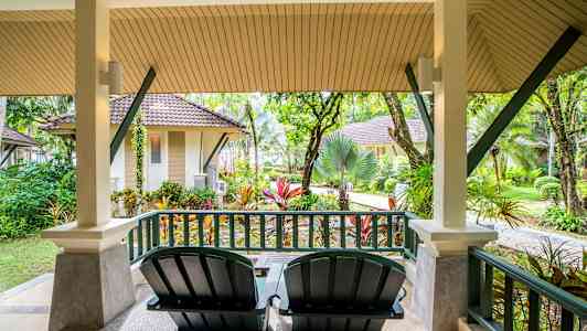 Veranta, jossa kaksi tuolia ja näkymä puutarhaan ja pieniin rakennuksiin. (Tekoälyn luoma teksti)