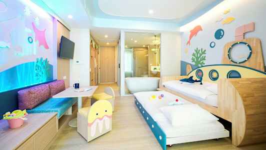 Värikäs perhehuone vedenalaisella teemalla, sisältäen vuoteita ja leikkialueen. (Tekoälyn luoma teksti)