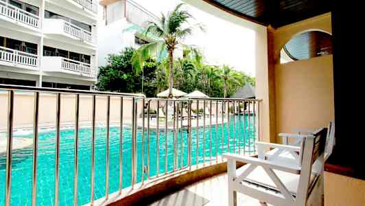 Näkymä parvekkeelta, jossa on valkoiset tuolit, kohti uima-allasta ja ympäröiviä rakennuksia. (Tekoälyn luoma teksti)