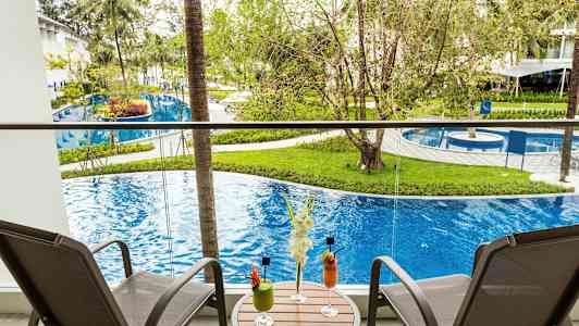 Parveke, jossa kaksi tuolia ja pöytä, jolla juomia, näköala altaalle ja vehreyteen. (Tekoälyn luoma teksti)