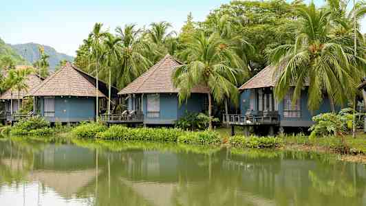 Useita sinisiä bungalowia olkikatolla sijaitsee vehreän lammen varrella palmujen ympäröimänä. (Tekoälyn luoma teksti)