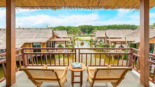 Kaksi tuolia ja pieni pöytä verannalla, josta on näkymä veteen rakennettuihin mökkeihin. (Tekoälyn luoma teksti)