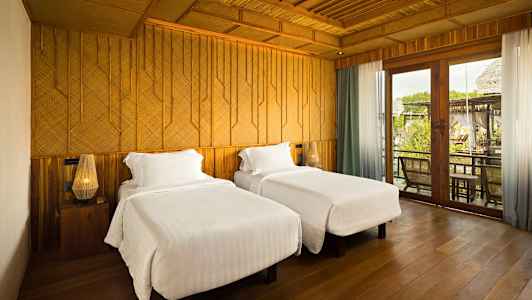 Kaksi sänkyä valkoisilla vuodevaatteilla sijaitsee huoneessa, jossa on puuyksityiskohtia ja suuret lasiovet. (Tekoälyn luoma teksti)