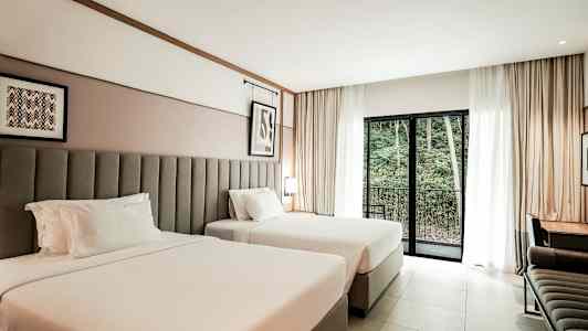 Hotellihuone, jossa on kaksi leveää sänkyä, kirjoituspöytä ja parvekkeen ovi näkymällä metsäalueelle. (Tekoälyn luoma teksti)