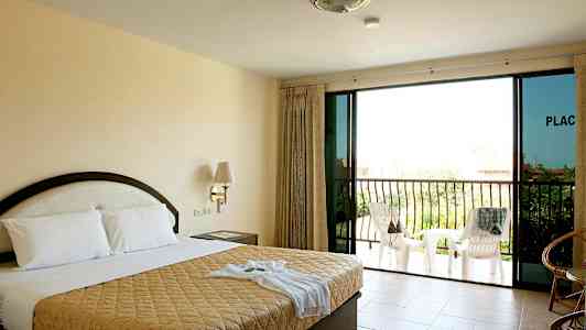 Hotellihuone, jossa on parivuode, yöpöytä, lasiovet ja parveke, jossa on tuoleja. (Tekoälyn luoma teksti)