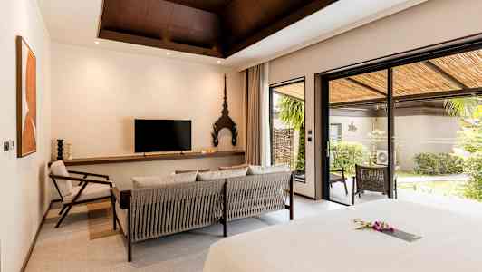 Hotellihuone, jossa moderni sisustus, istuinryhmä, televisio sekä suuret lasiovet, jotka johtavat vehreälle terassille. (Tekoälyn luoma teksti)