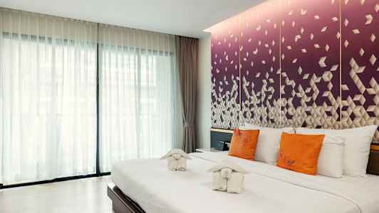 Hotellihuone, jossa suuri sänky, valkoiset vuodevaatteet, oranssit tyynyt ja koristeelliset pyyhkeet. Taustalla näkyy violetti seinä geometrisella kuviolla. (Tekoälyn luoma teksti)